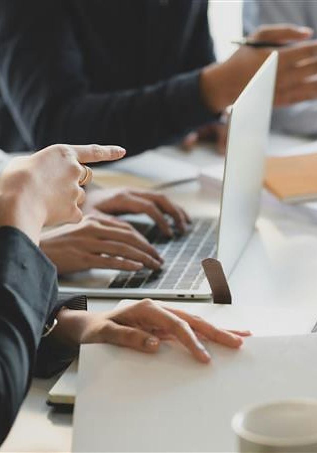 eople working together at a desk with laptops and notebooks during a meeting.